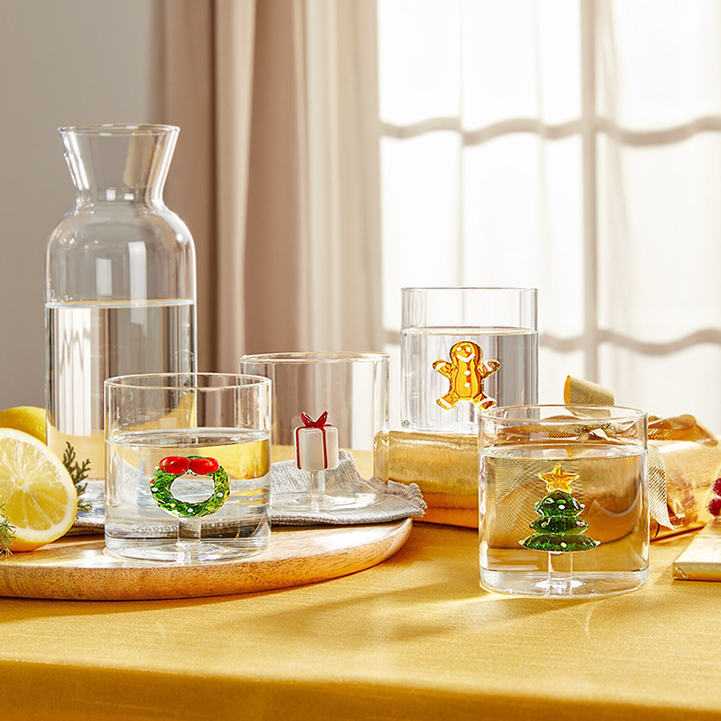 Ein Tisch mit einer Karaffe und vier Wassergläsern, die jeweils mit festlichen Motiven verziert sind: einem Kranz, einem Geschenk, einem Lebkuchenmann und einem Weihnachtsbaum.