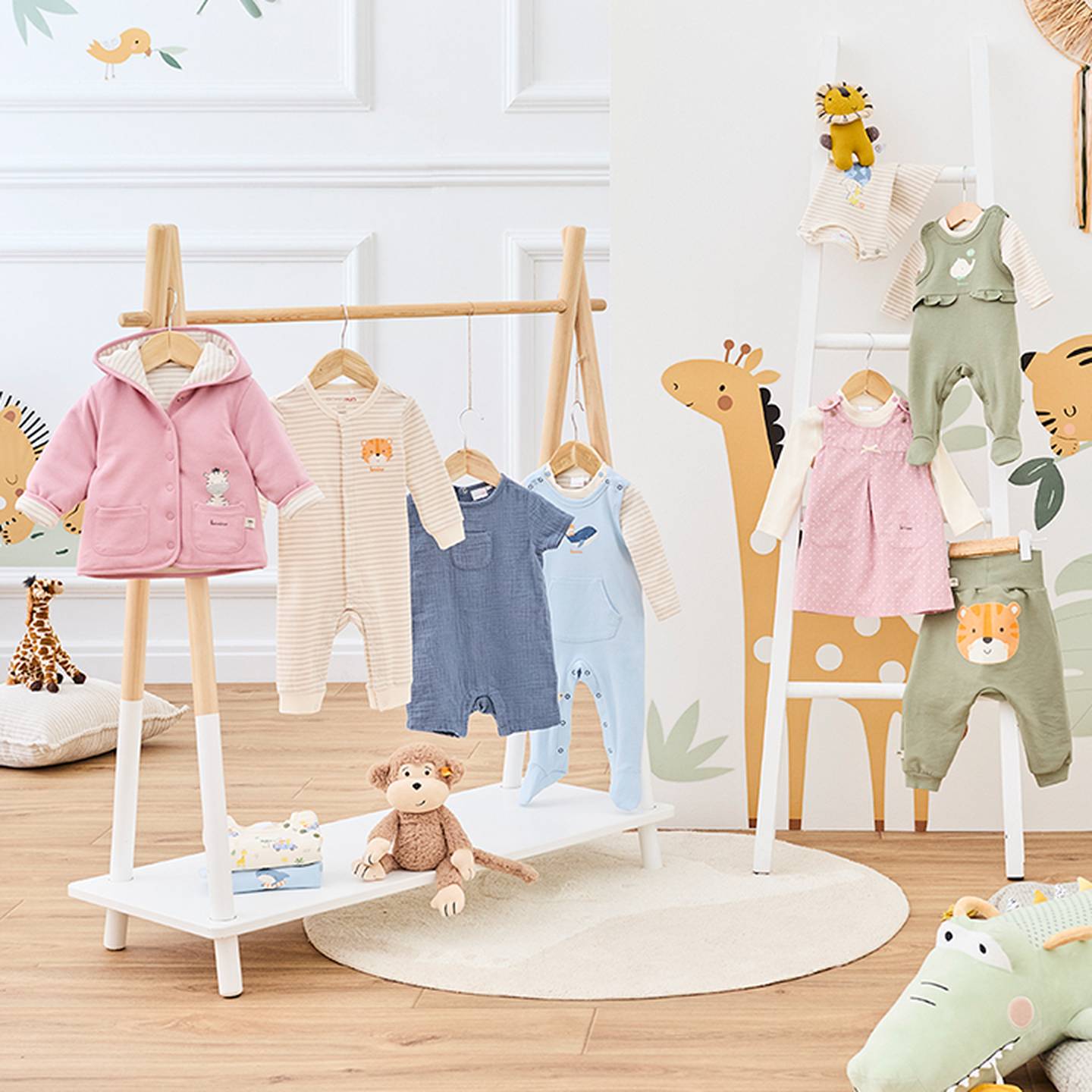 Kinderbekleidungsauslage mit Giraffenmotiven, mit pastellfarbenen Stramplern und Outfits an Kleiderstangen sowie Plüschtieren auf einem Holzboden.