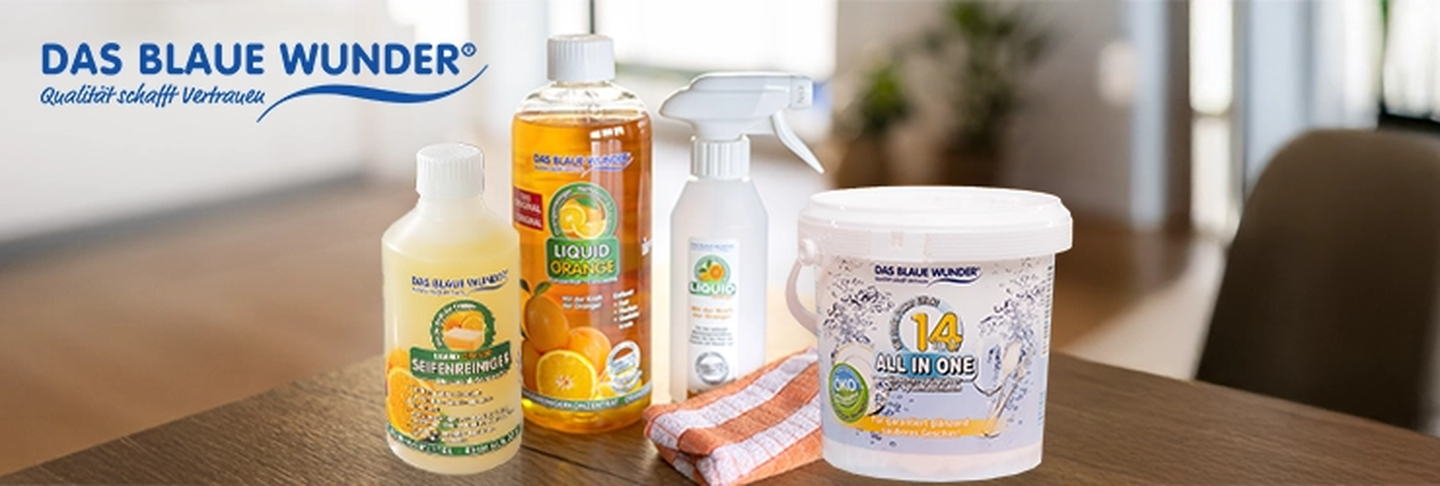 Cleaning products from Das Blaue Wunder, including sprays, a liquid cleaner, and a tub, displayed on a wooden table.