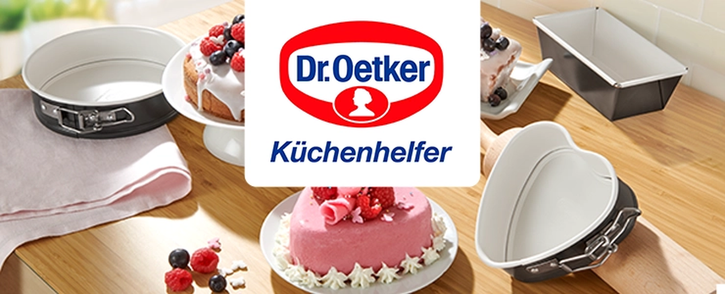 Verschiedene Kuchen auf einem Holztisch mit Backformen, verziert mit Beeren. In der Mitte das Logo von „Dr. Oetker Küchenhelfer“. Rechts ein Tortenständer.
