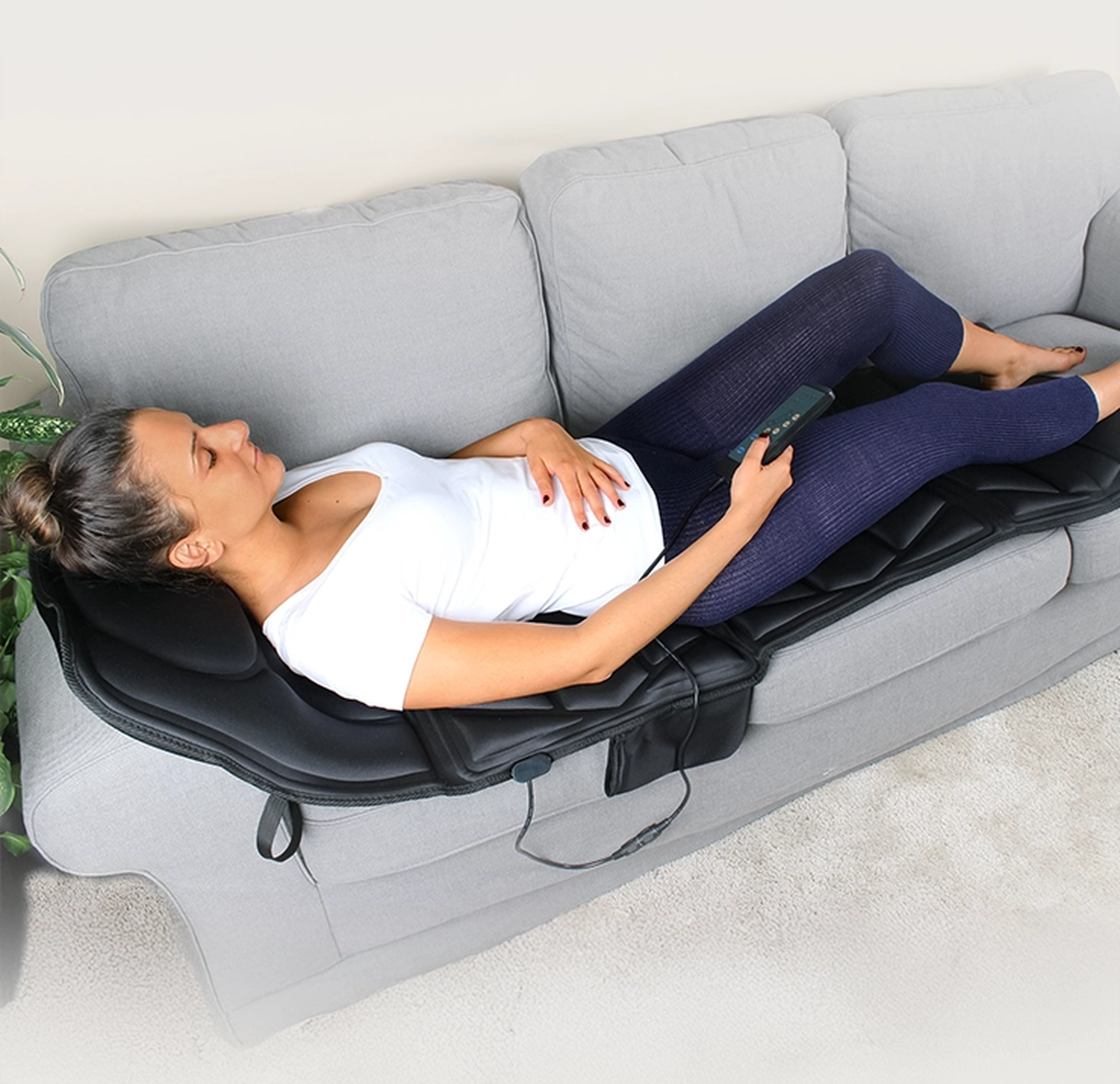 Eine Frau liegt entspannt auf einer Massagematte auf einem grauen Sofa