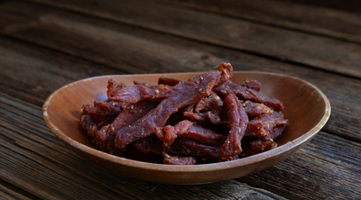 Trockenfleisch, das in dünnen Streifen in einer Holzschale liegt.