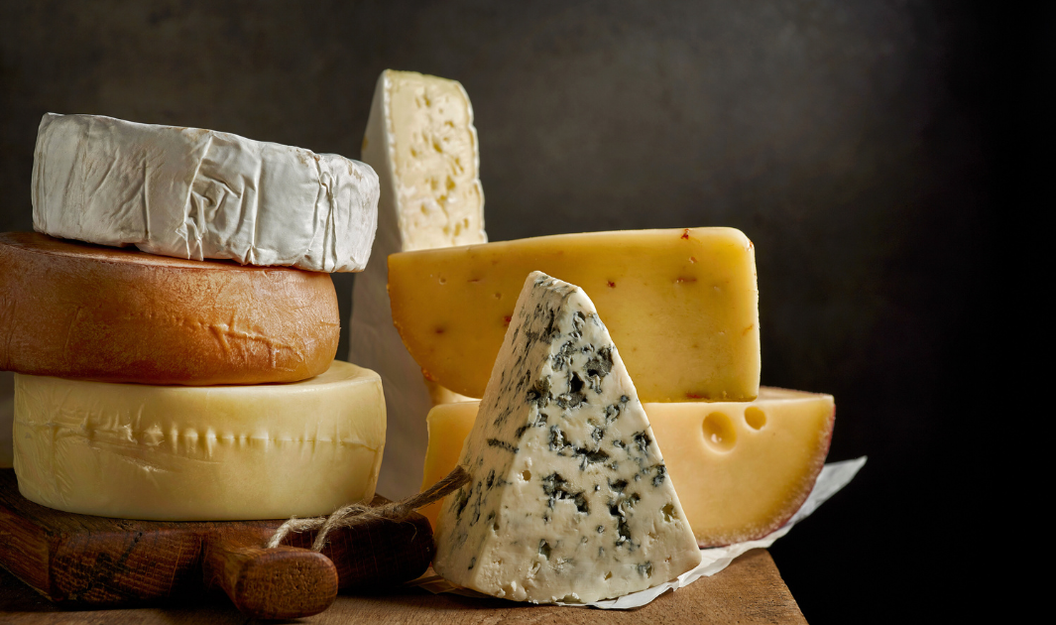 Unterschiedliche Käsesorten liegen gestapelt auf einem Holzbrett