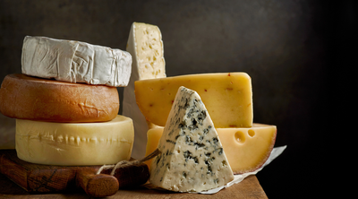 Unterschiedliche Käsesorten liegen gestapelt auf einem Holzbrett