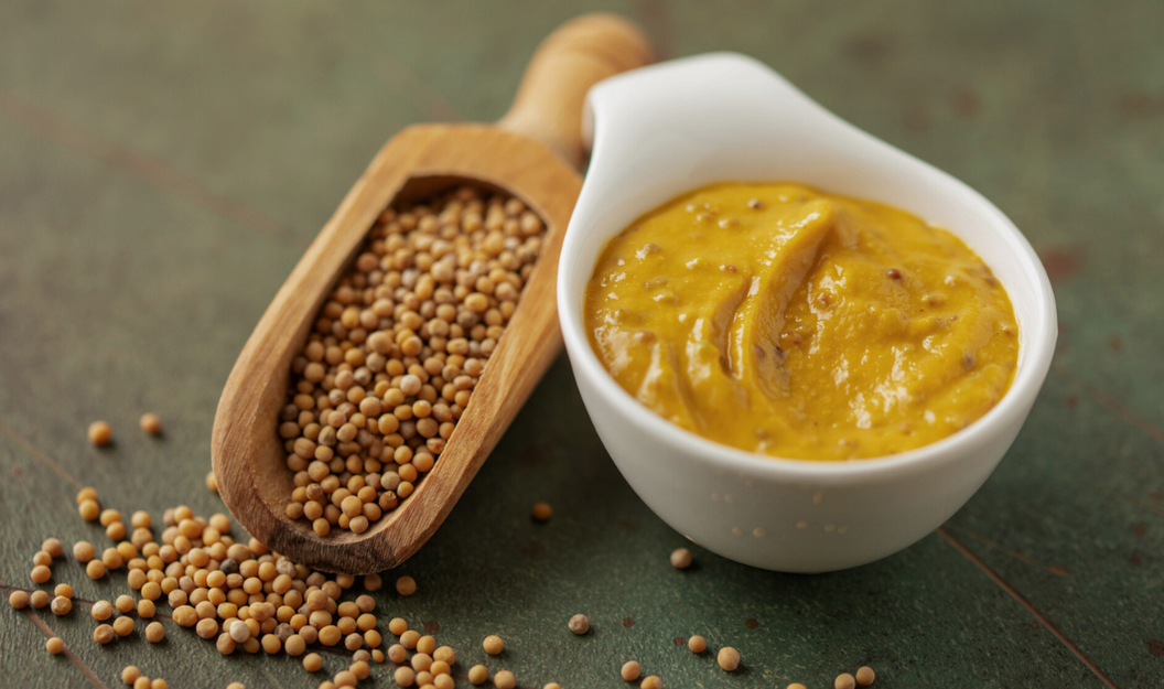 Senfkörner in einer Gewürzschaufel und Senf in einer Schale