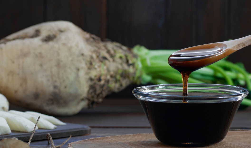 Flüssiger Zuckerrübensirup vor einer ganzen und zerkleinerten Rübe.