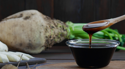 Flüssiger Zuckerrübensirup vor einer ganzen und zerkleinerten Rübe.