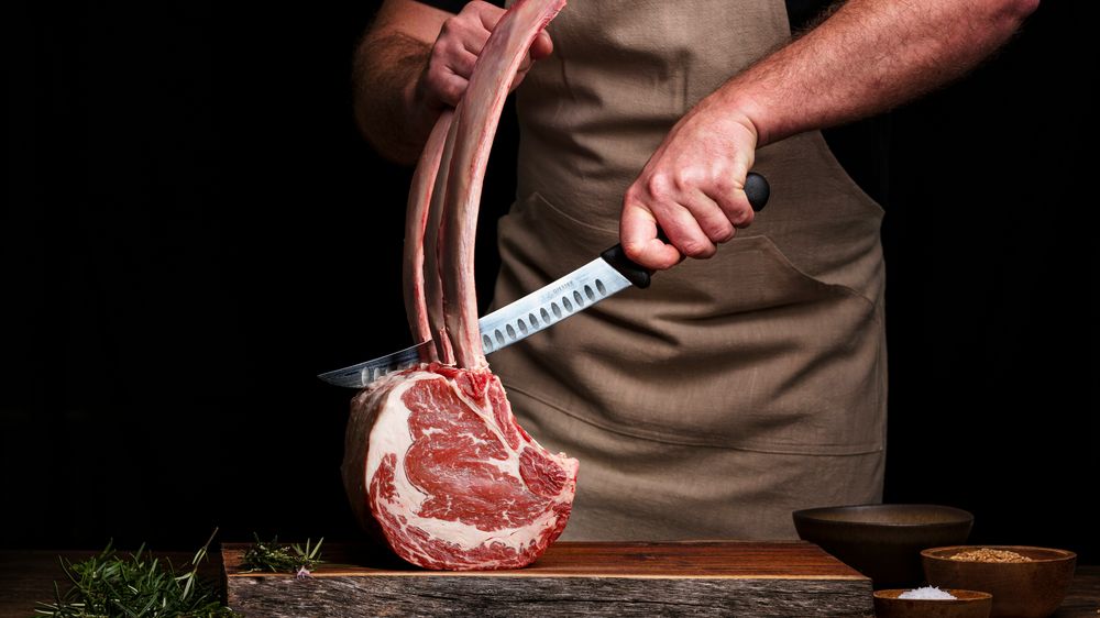 Person schneidet großes Stück Fleisch zwischen zwei Knochen