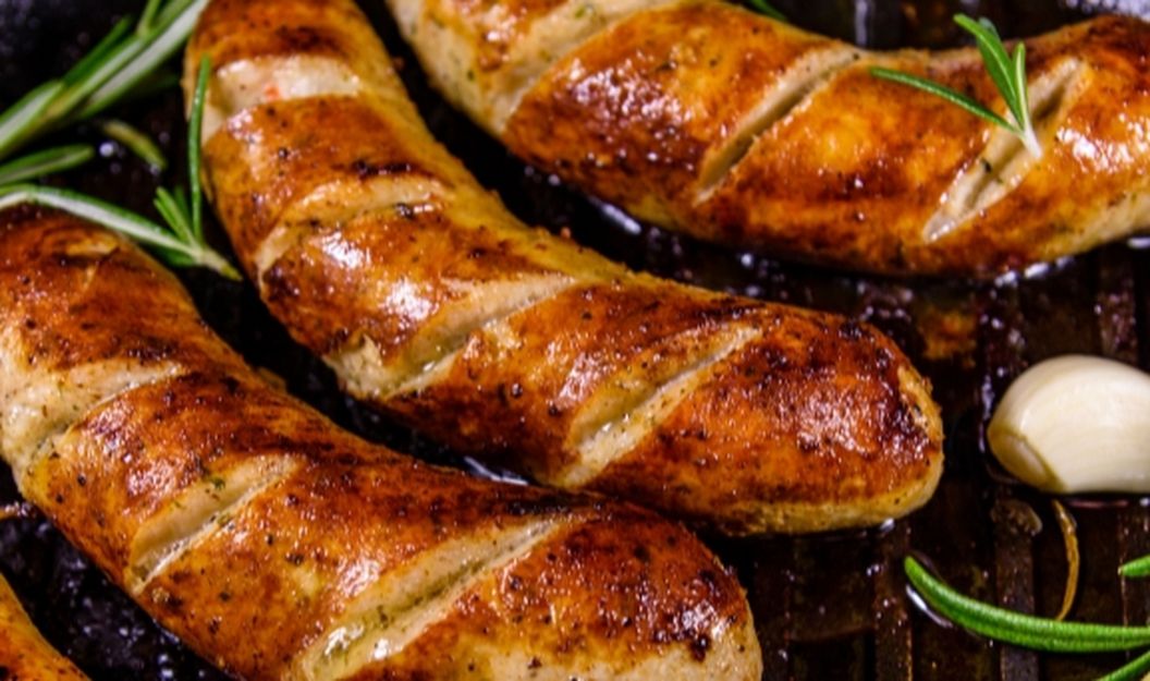 Bratwürste brutzeln dicht an dicht mit Gewürzen auf dem Grill.