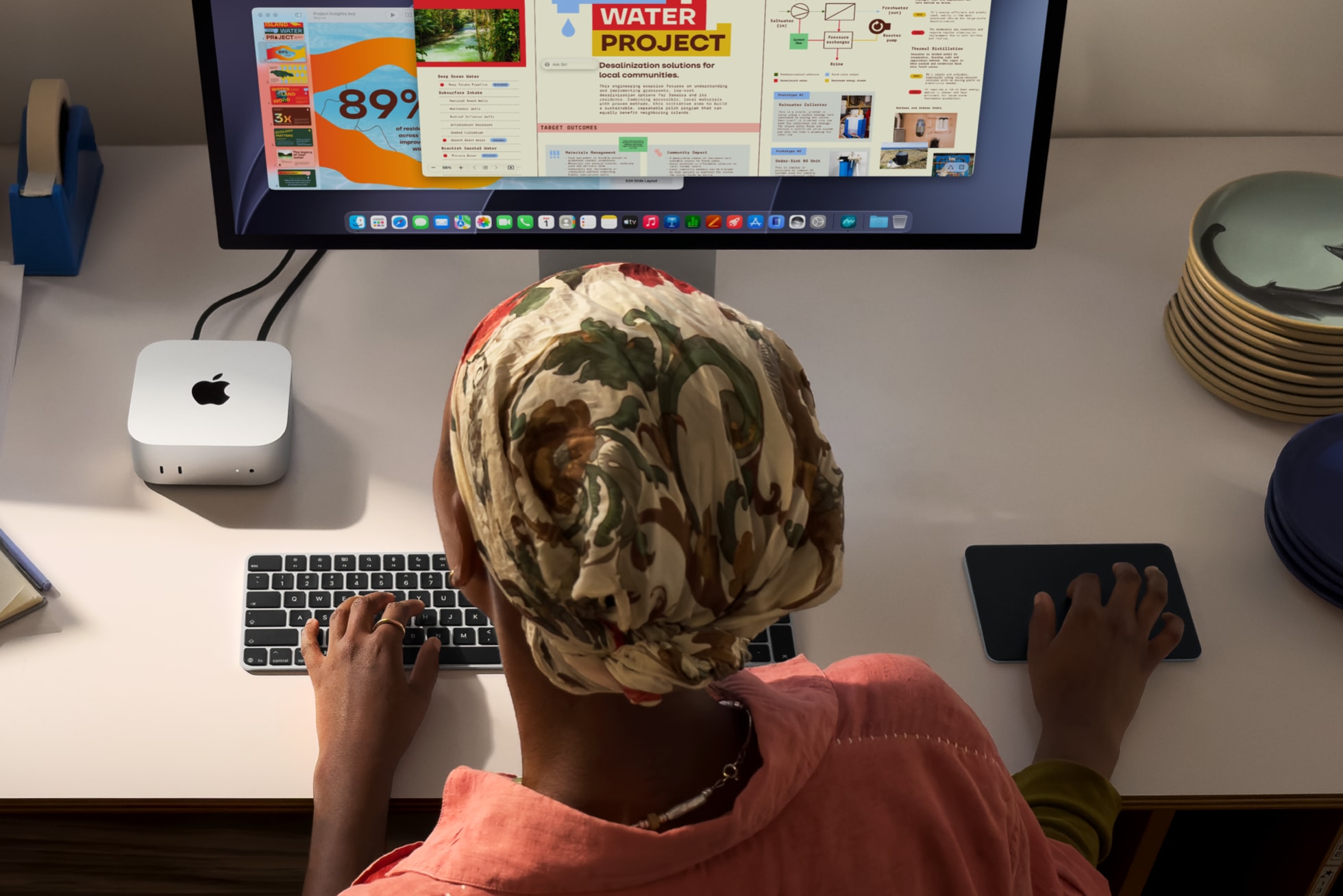 Person using a Mac Mini and typing on a keyboard, looking at a computer monitor displaying a "Water Project" webpage.