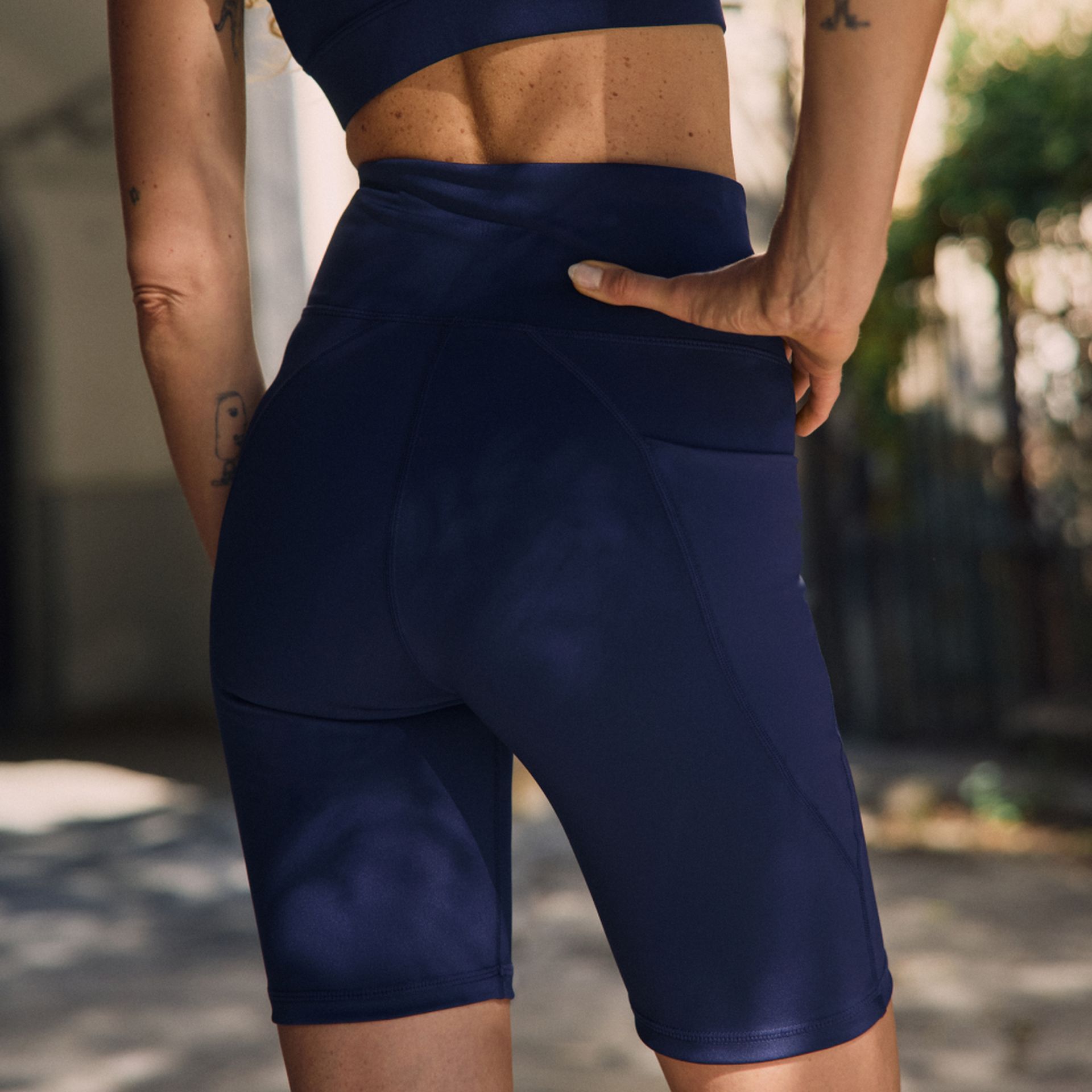 A person wearing high-waisted navy blue athletic shorts and a matching top stands outdoors, one hand on their hip.