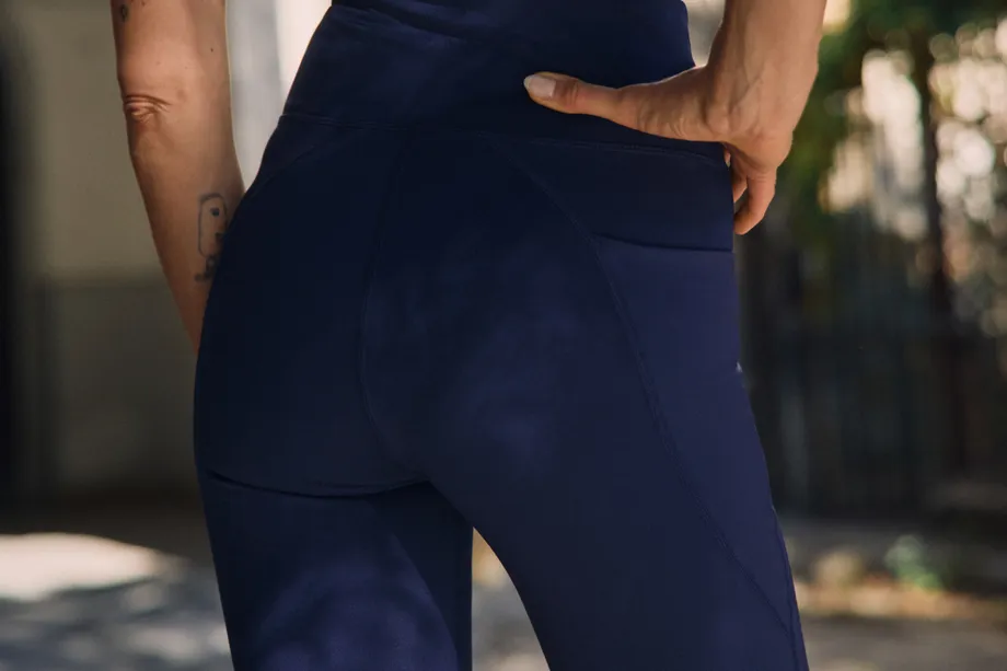A person wearing high-waisted navy blue athletic shorts and a matching top stands outdoors, one hand on their hip.