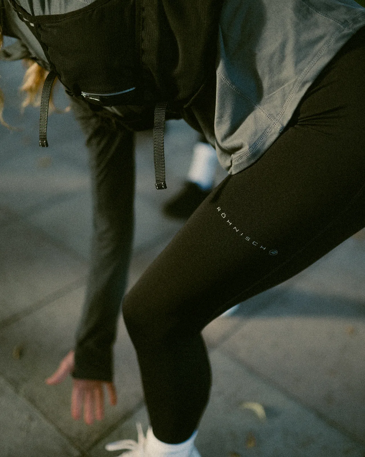 Person in athletic wear stretching outdoors on a paved surface, wearing black leggings and white sneakers.