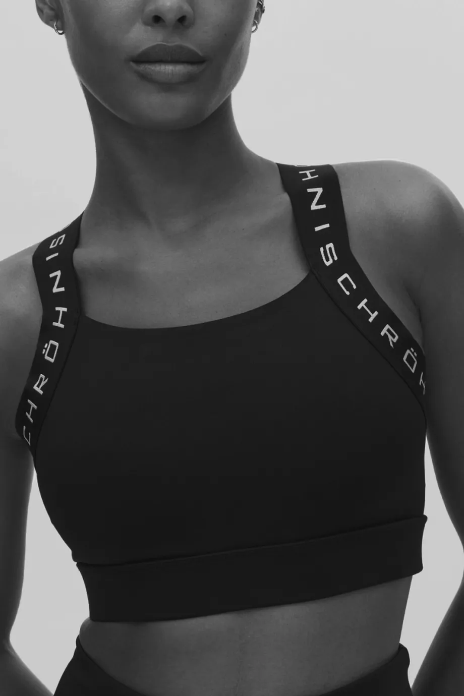 Person wearing a black sports bra with branded straps, against a plain background.