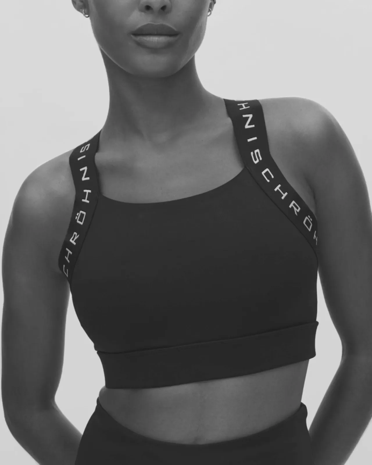 Woman wearing a black sports bra with branded straps, standing against a plain background, posing confidently.