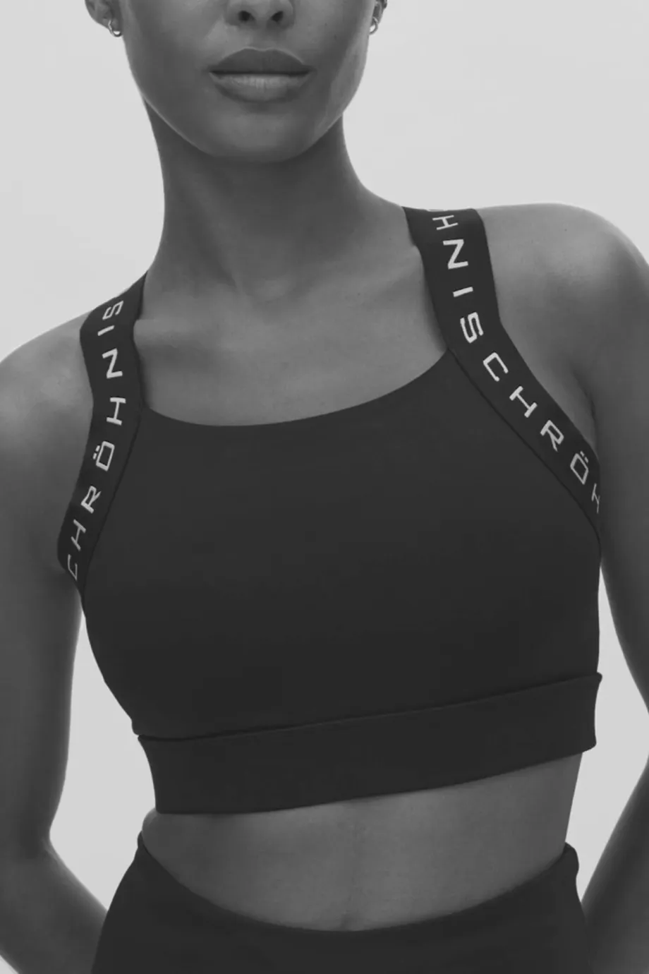 Woman wearing a black sports bra with branded straps, standing against a plain background, posing confidently.
