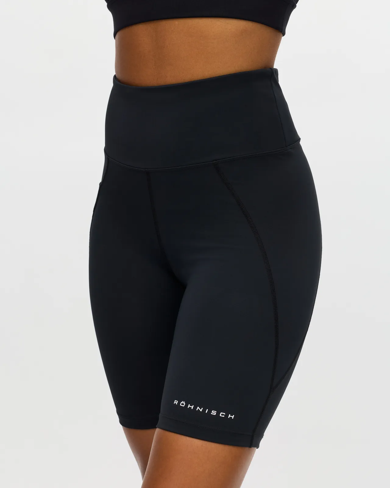 Person wearing black high-waisted athletic shorts and a matching crop top, shown from waist to mid-thigh, with branding on the left leg.