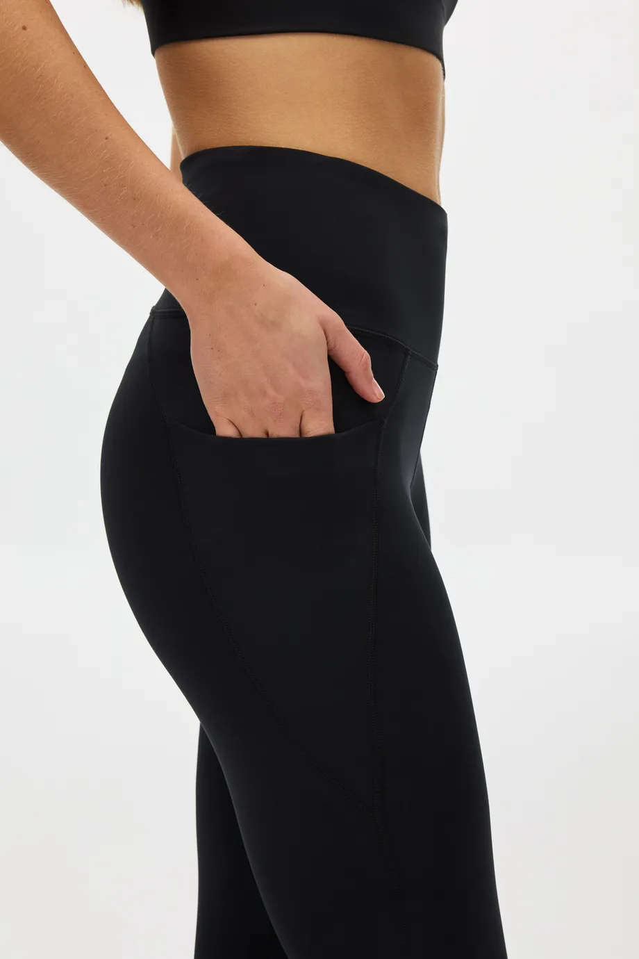 Person wearing black athletic leggings with a hand in the side pocket, showcasing a high waistband and a partial view of a black top.