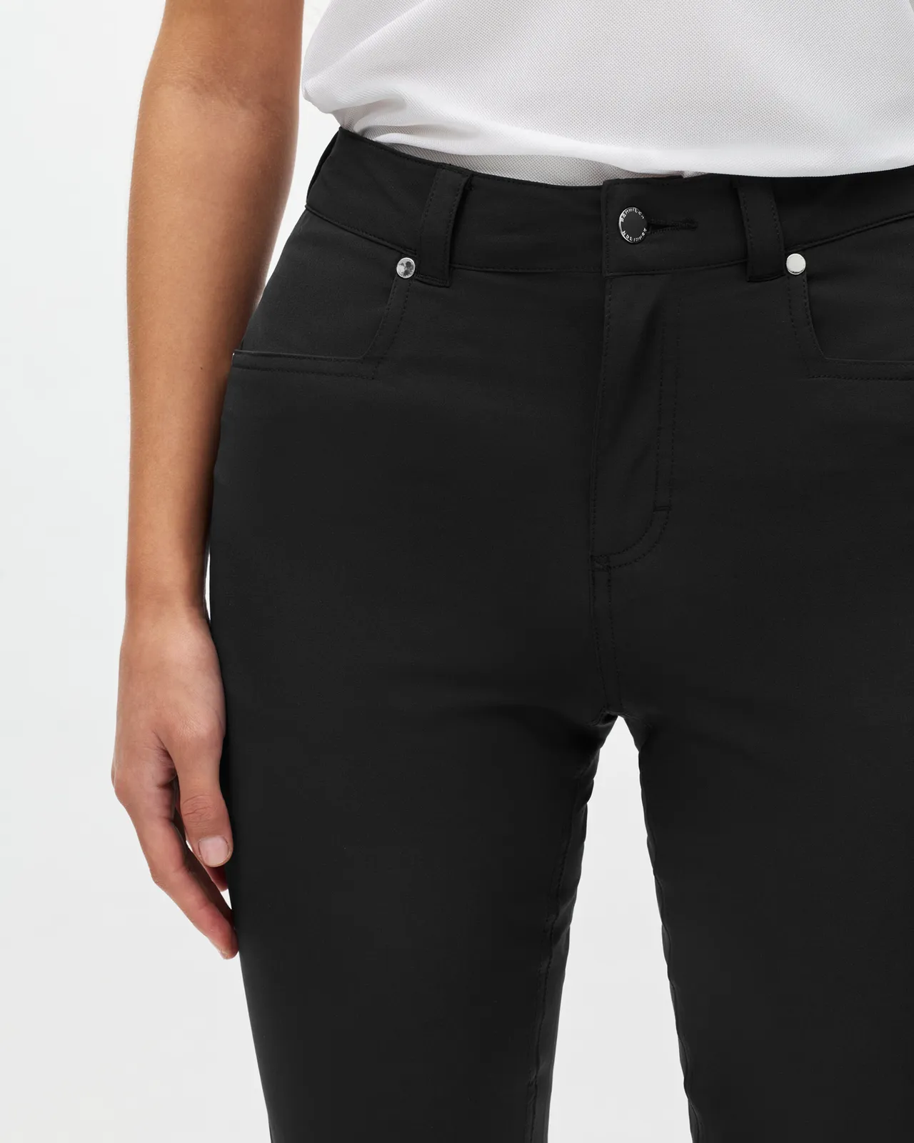 Person wearing black high-waisted pants with a white top, hand relaxed at their side, on a plain background.