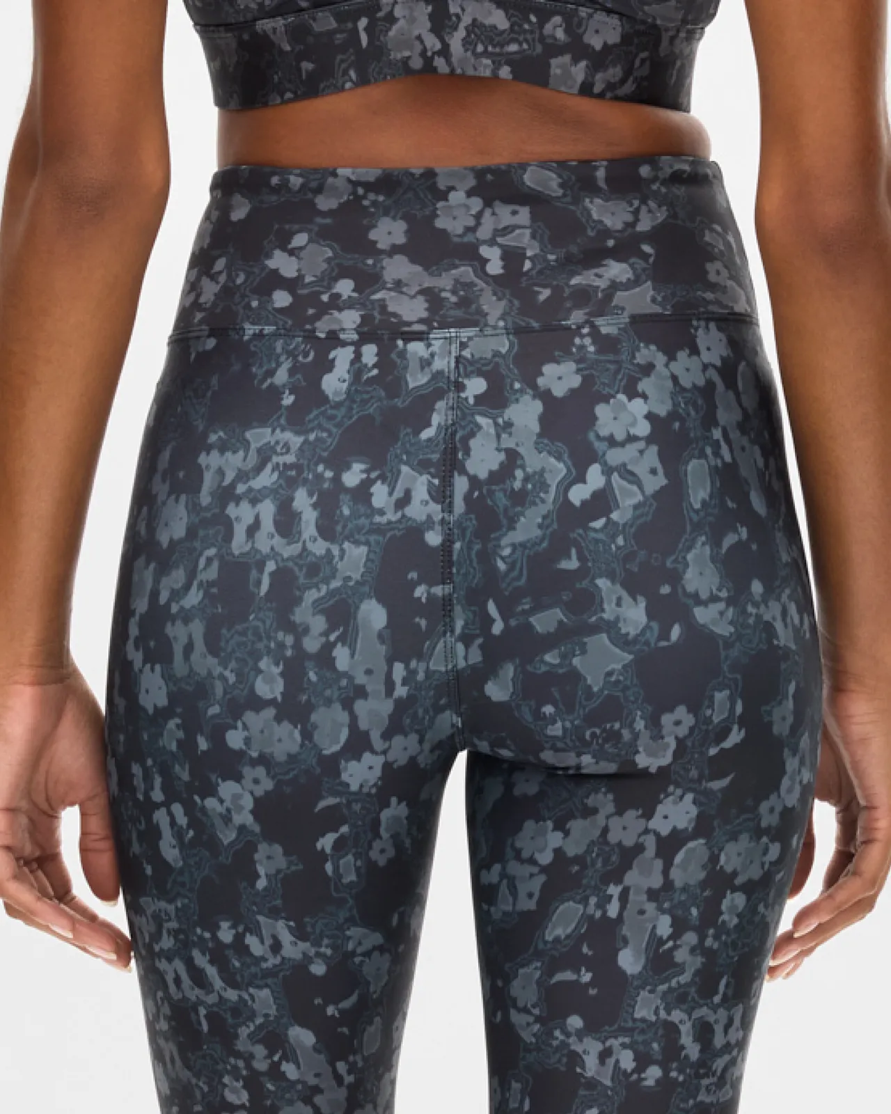 Person wearing a black and gray floral-patterned sports bra and leggings, viewed from the back, against a plain white background.
