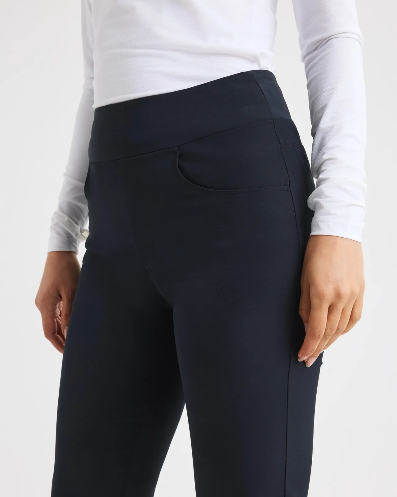 Person wearing a white long-sleeve top and dark high-waisted pants, standing against a plain background.