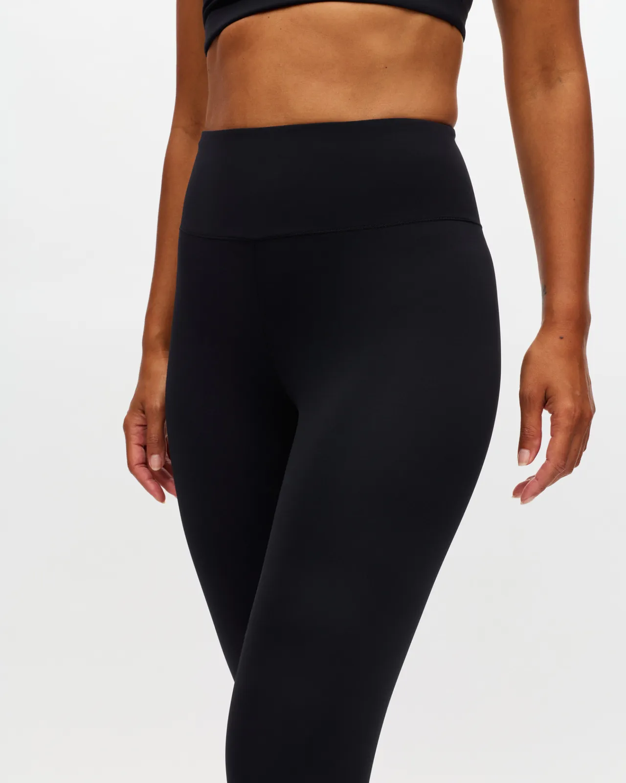 Person wearing a black sports bra and high-waisted leggings, showing a fit and toned midsection against a plain background.