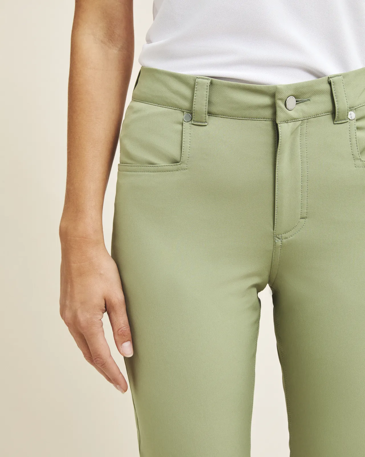 Person wearing light green pants and a white shirt, with a focus on the pants and one hand visible by their side.
