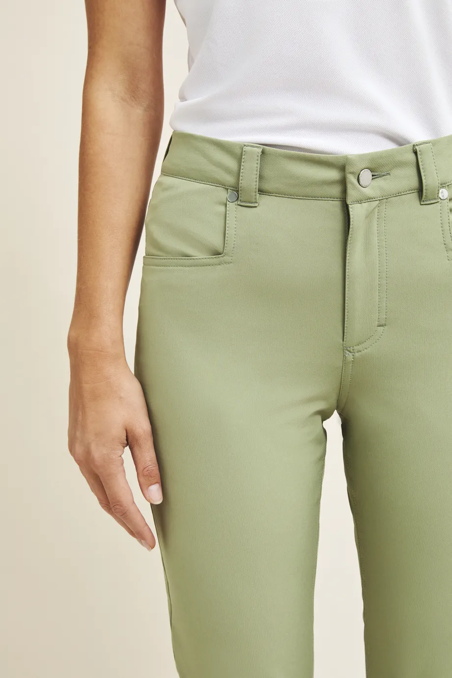 Person wearing light green pants and a white shirt, with a focus on the pants and one hand visible by their side.