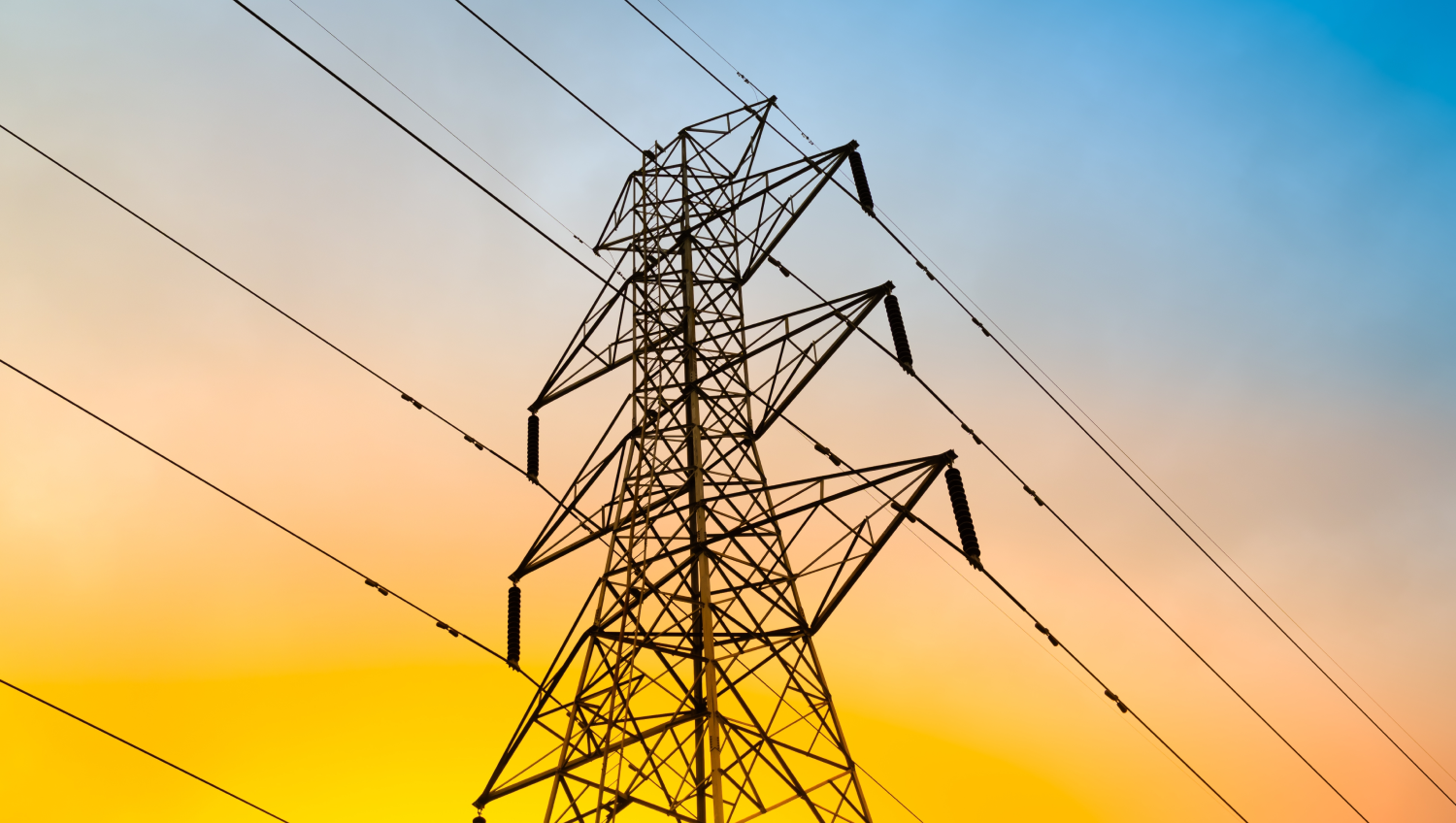 Strommast mit Übertragungsleitungen vor einem Sonnenuntergang.