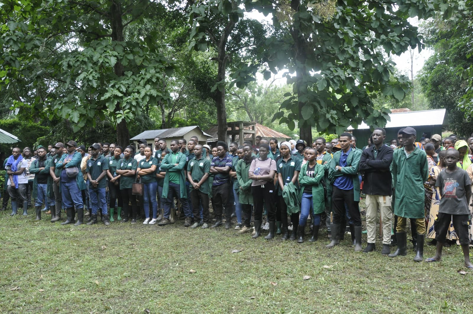 A group of people standing all together in front of houses and surrounded by trees