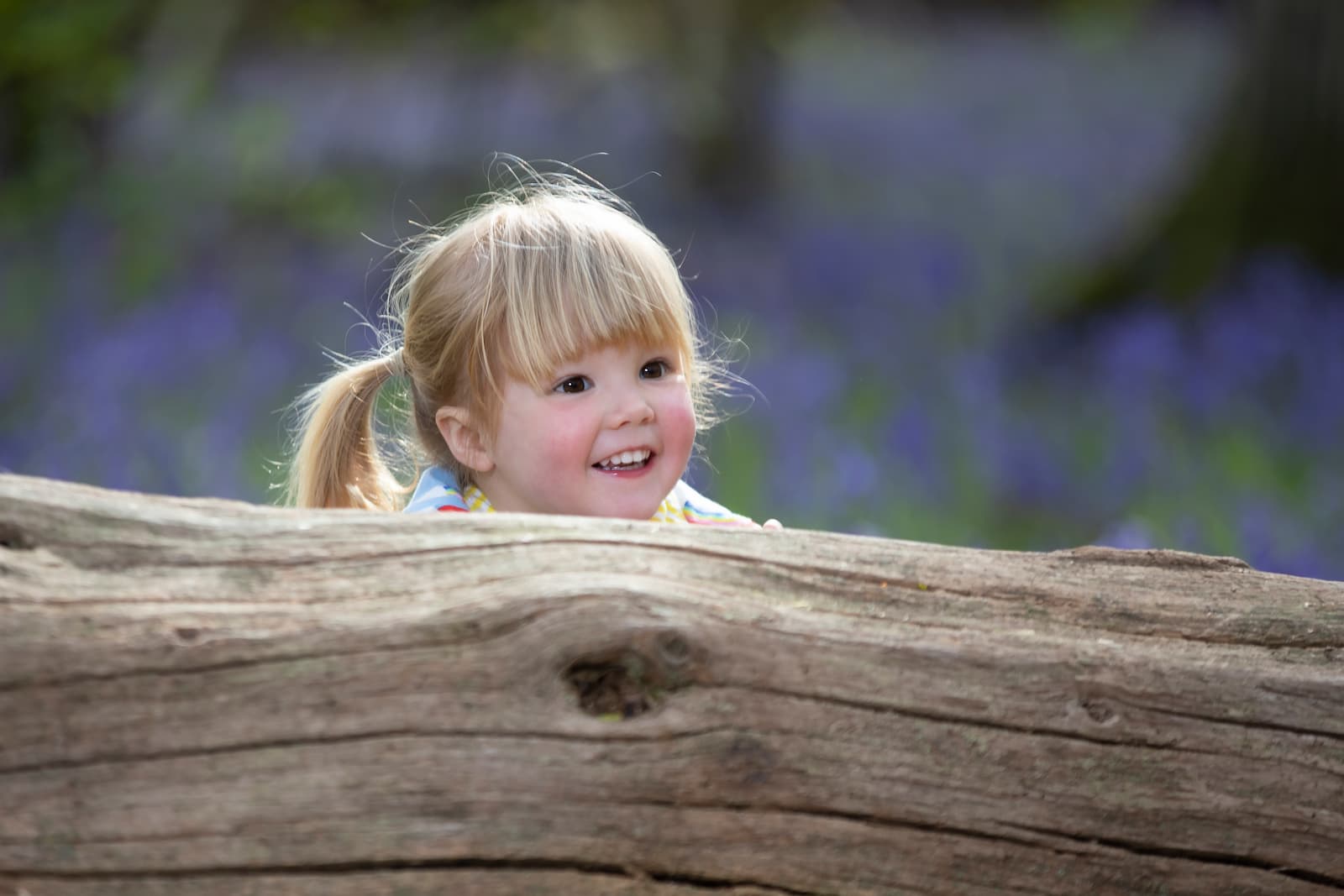 A child peeking up from behind a log
