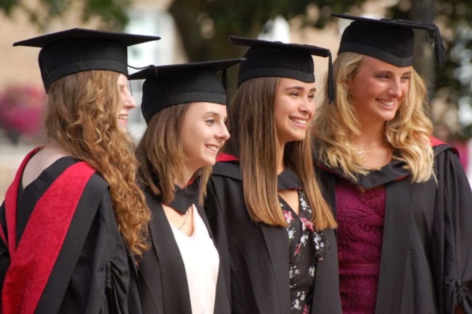 Graduates Four women in graduation gowns and caps smile, standing outdoors, celebrating their achievement.