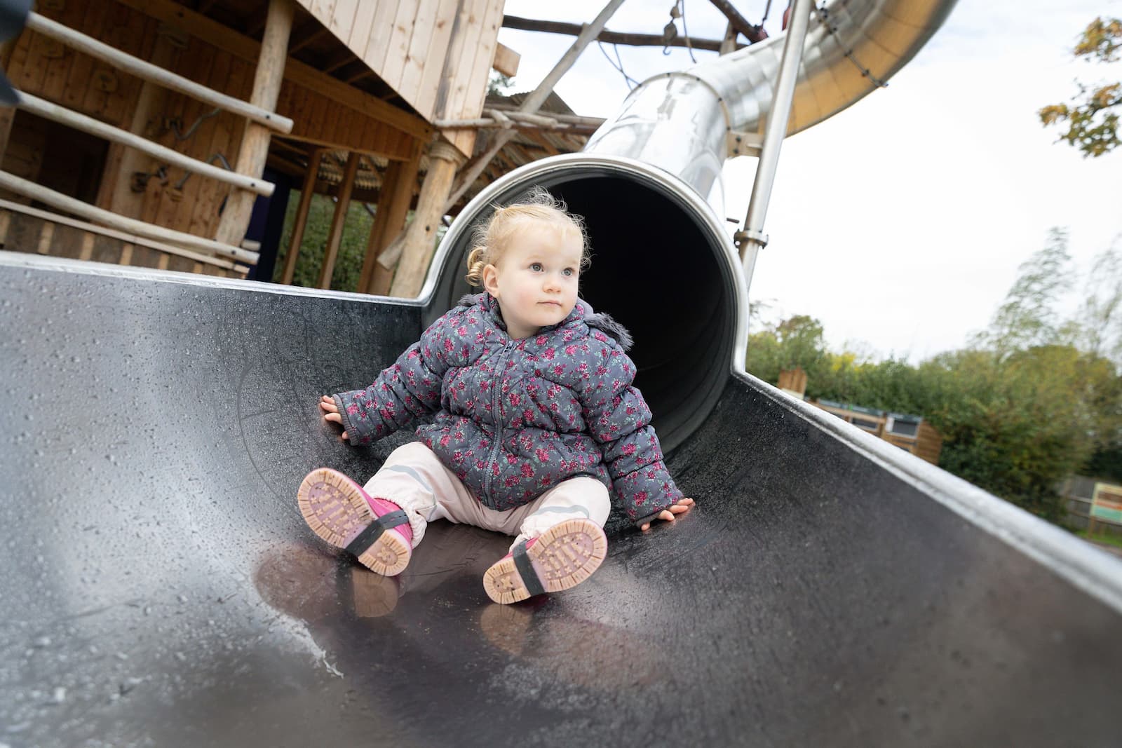 A child sat at the end of a long metal slide in a play area
