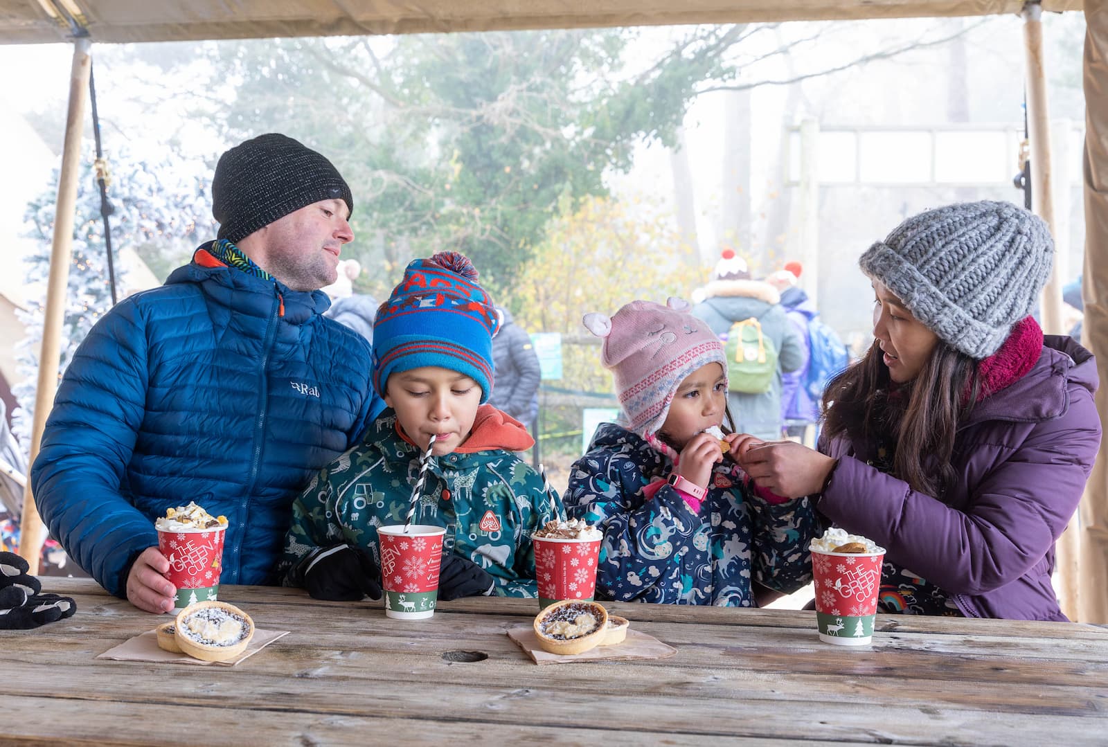 A family sit at a bench enjoying festive food and drinks