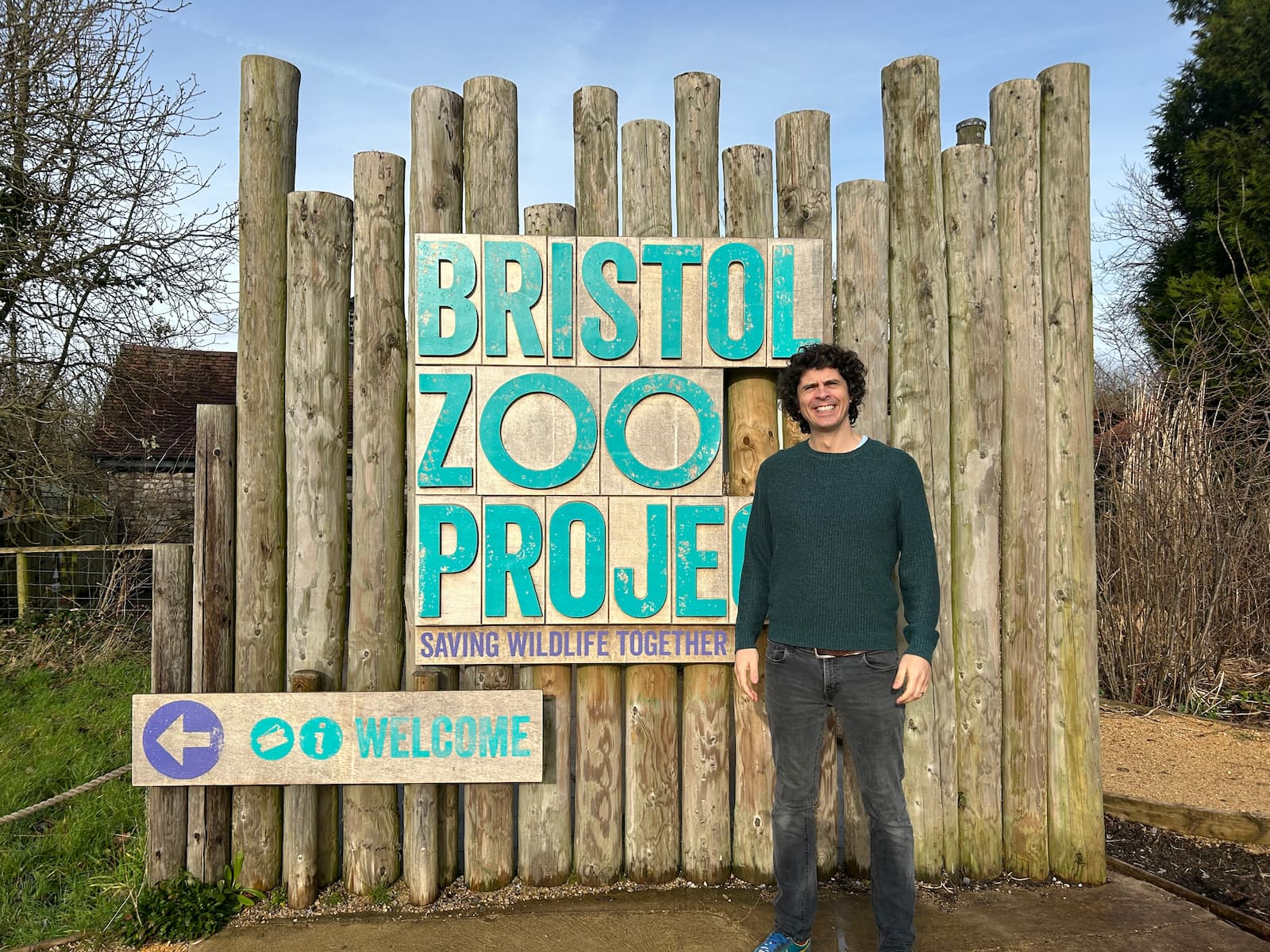 An individual stands in front of a wooden Bristol Zoo Project sign