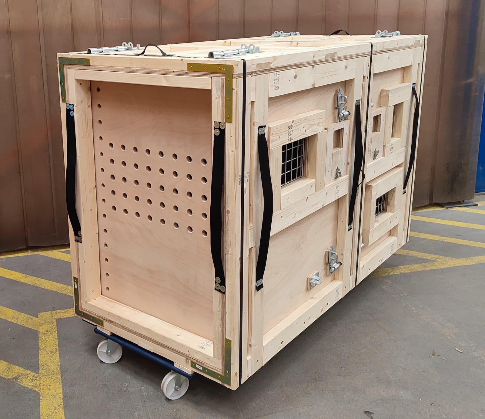 Gorilla transport crate A large wooden crate with ventilation holes and metal latches, placed on a wheeled platform in an industrial setting.