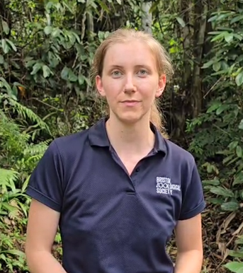 Woman standing in forest wearing blue polo shirt from Bristol Zoological Society
