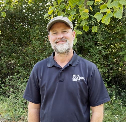 A man with a beard and cap smiles, wearing a black 