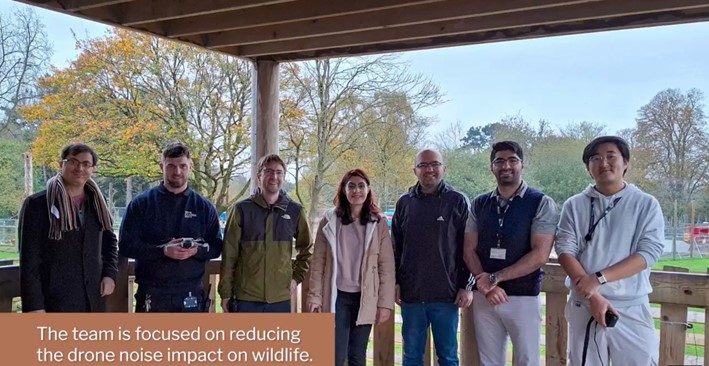Seven people standing infront of the giraffe habitat at Bristol Zoo Project holding drones - caption reads 