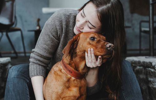 Frau, die liebevoll einen braunen Hund in Innenräumen kuschelt, beide wirken zufrieden und entspannt.