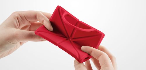 Zwei Hände die einen roten Silikon Falt-Reisenapf zusammenfalten.