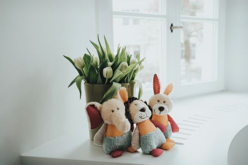 Drei Plüschtiere sitzen auf einer weißen Fensterbank neben einer Vase mit weißen Tulpen am Fenster.