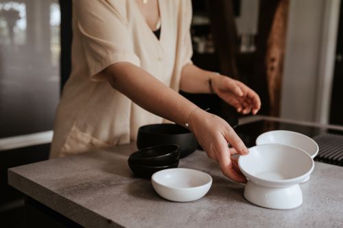 Person in hellen Kleidern ordnet schwarze und weiße Futternäpfe auf einer Küchenarbeitsplatte an; Fokus auf den Händen und den stilvollen Schalen.