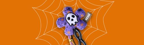 Eine schwarze und lilafarbene Katzernangel mit Blumenform und mit einem Totenkopf-Motiv auf orangefarbenem Hintergrund und einem weißen Spinnennetz-Muster.