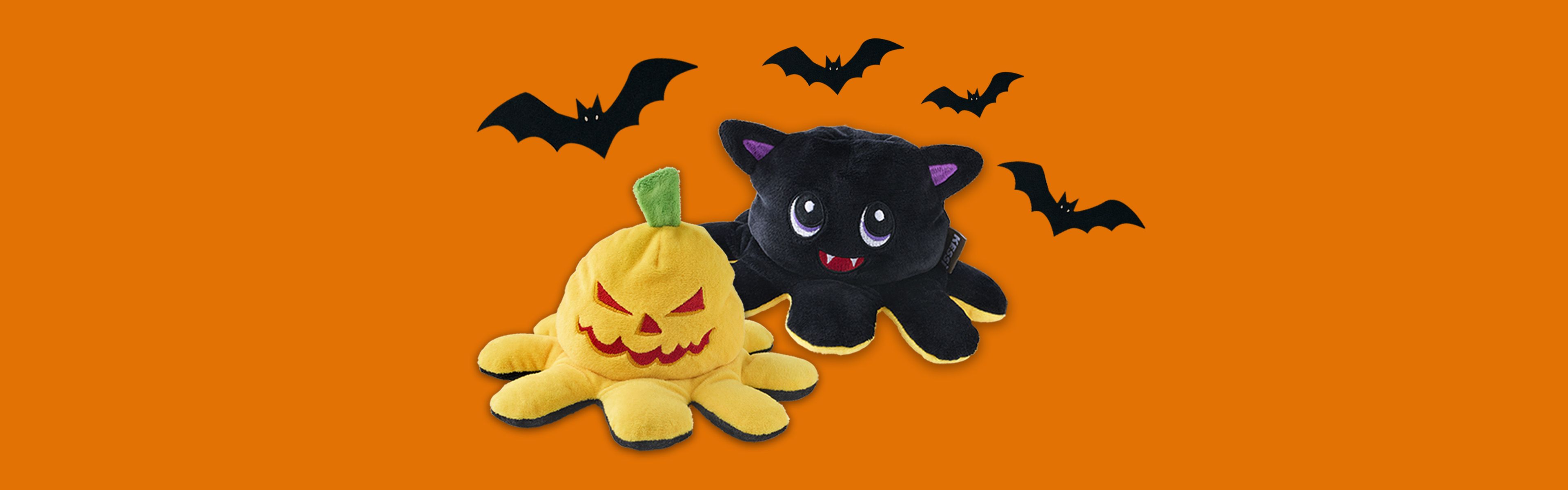 Niedliche Plüschtiere in Form eines gelben Kürbisses und einer schwarzen Fledermaus, über denen Fledermäuse fliegen, vor einem orangefarbenen Hintergrund.