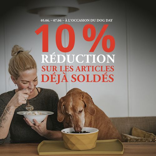 Visuel promotionnel avec un texte rouge et blanc : « 05/06 – 07/06 – À L´OCCASION DU DOG DAY : 10 % RÉDUCTION SUR LES ARTICLES DÉJÀ SOLDÉS » En arrière-plan, on voit une photo réaliste d’une femme et d’un chien assis à une table en train de manger quelque chose. La femme regarde joyeusement son chien.