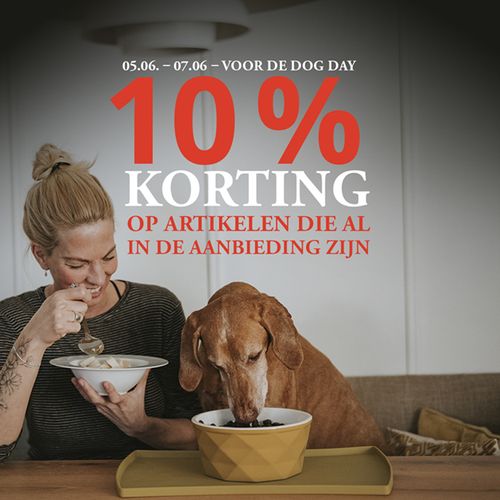 Actiebeeld met rood-witte tekst: “05-06 – 07-06 – VOOR DE DOG DAY: 10% KORTING OP ARTIKELEN DIE AL IN DE AANBIEDING ZIJN” Op de achtergrond staat een realistische foto van een vrouw en een hond die aan een tafel zitten en iets eten. De vrouw kijkt haar hond blij aan.