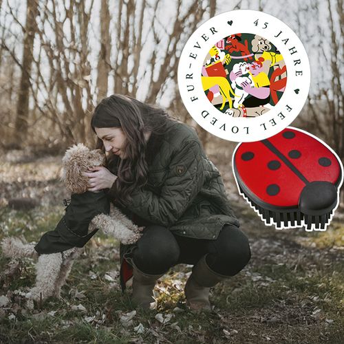 Frau kniet im Freien und umarmt einen Hund, neben ihr liegen eine Bürste in Marienkäferform und ein buntes kreisförmiges 45 Jahre Logo.