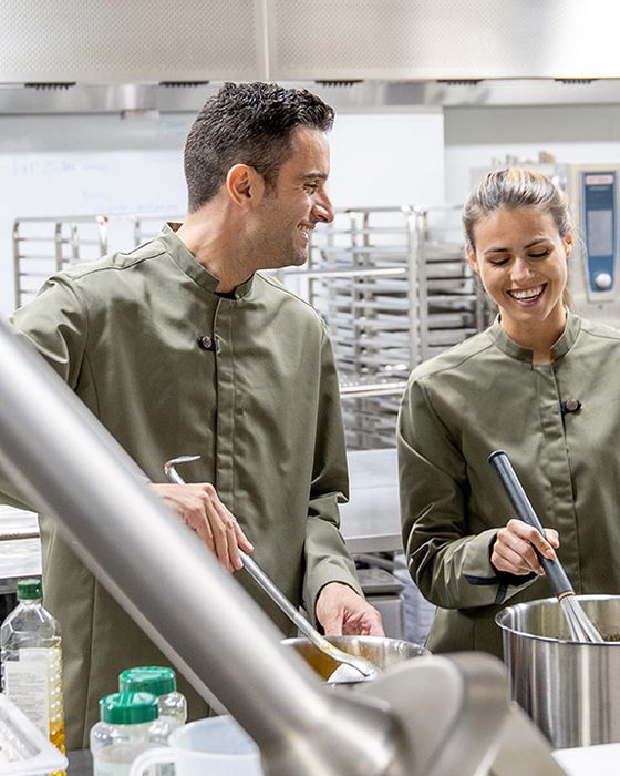 Hospitality and kitchen workers wearing Alsico uniforms, preparing food in a kitchen.