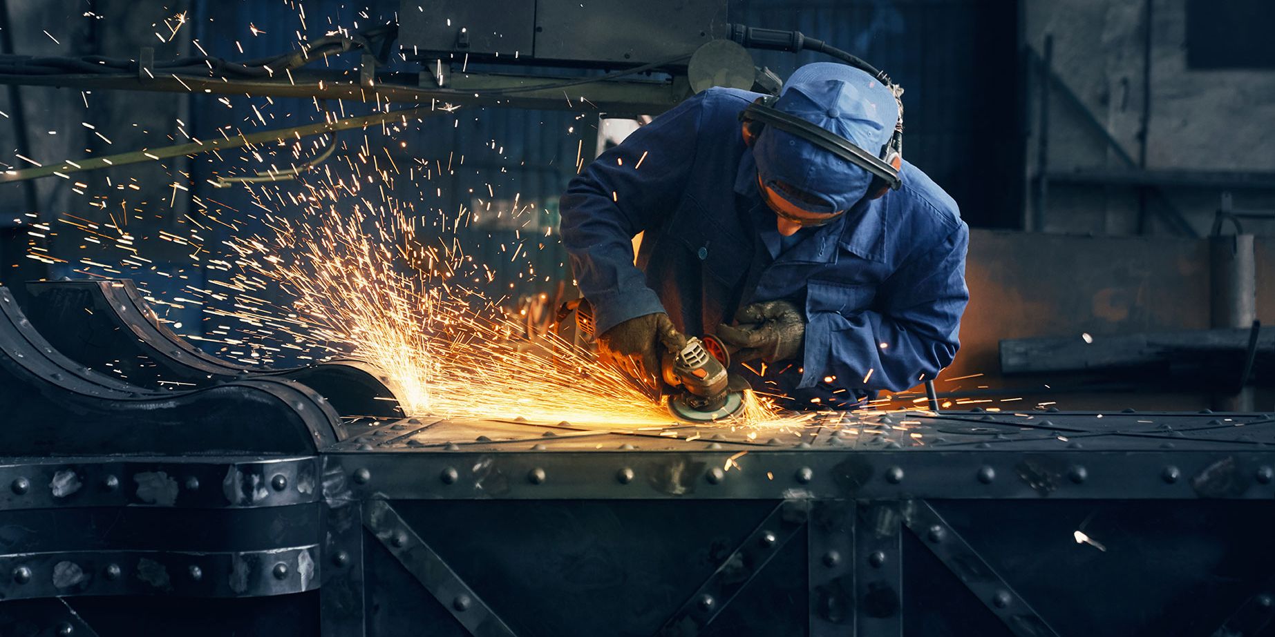 Bright sparks flying from industrial metalwork, highlighting welding PPE and safety gear.